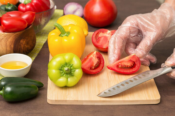 Chef cutting tomato and different vegetables for salad close up. Hands in gloves with knife cooking vegetable, healthy vegetarian vegan diet food