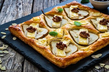 Baked puff pastry with pear and camembert cheese on baking paper on wooden table
