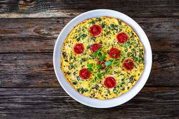 Omelette  - scrambled eggs with oregano, thyme, spinach and cherry tomatoes on wooden table