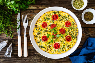 Omelette  - scrambled eggs with oregano, thyme, spinach and cherry tomatoes on wooden table
