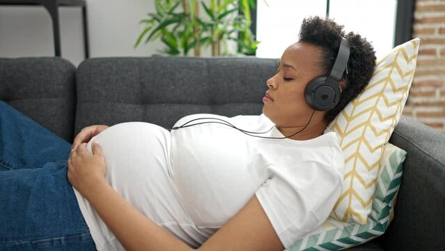 Young pregnant woman listening to music sleeping on sofa at home