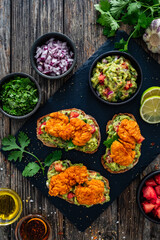 Tasty bruschetta with chicken nuggets, guacamole,  tomato, and onion on wooden table
