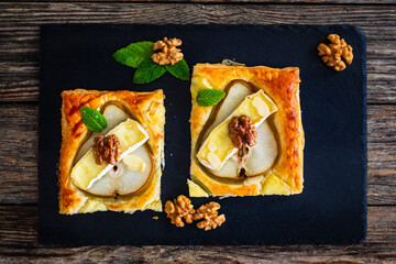 Baked puff pastry with pear and camembert cheese on baking paper on wooden table
