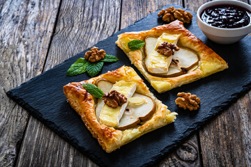 Baked puff pastry with pear and camembert cheese on baking paper on wooden table
