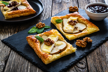 Baked puff pastry with pear and camembert cheese on baking paper on wooden table

