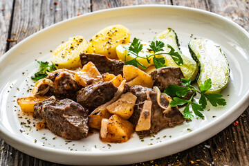 Fried liver with apples, potatoes and onion on wooden table

