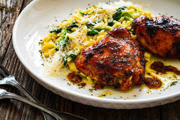 Greek style roasted chicken thighs with kritharaki rice and spinach on wooden table
