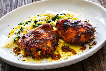 Greek style roasted chicken thighs with kritharaki rice and spinach on wooden table
