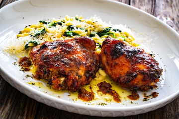 Greek style roasted chicken thighs with kritharaki rice and spinach on wooden table
