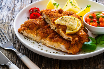 Crispy breaded seared chicken cutlet with boiled potatoes and vegetables on wooden table
