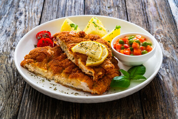 Crispy breaded seared chicken cutlet with boiled potatoes and vegetables on wooden table
