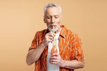 Senior man drinking cocktail from straw, eyes closed isolated on beige background