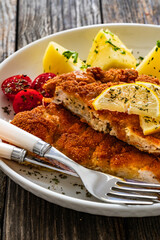 Crispy breaded seared chicken cutlet with boiled potatoes and vegetables on wooden table
