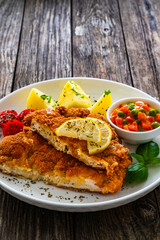 Crispy breaded seared chicken cutlet with boiled potatoes and vegetables on wooden table
