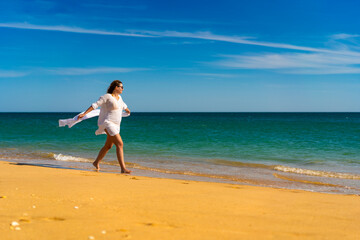 Fototapeta na wymiar Beach holiday - beautiful woman walking on sunny beach holding shawl 