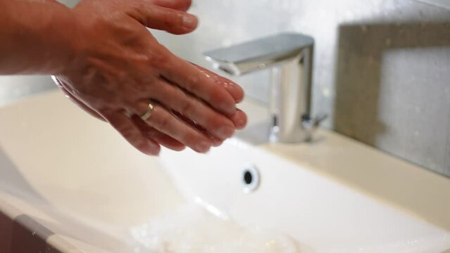 Slow Motion. Closeup of Human Hand Under Stream of Pure Water From Tap. Modern faucet in the bathroom. A man washes his hands under running water. Close-up