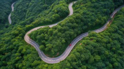 Aerial view of a winding countryside road passing through the green forest and mountain. red car is passing through.