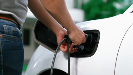 Progressive man attaches an emission-free power connector to the battery of electric vehicle at his...