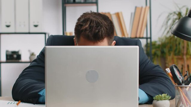 Confident young businessman hiding behind laptop computer, looking at camera, spying his colleagues working, peeping. Professional freelancer man looking from behind computer with cunning eyes glance