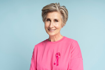 Portrait of confident smiling senior woman wearing pink t shirt with pink ribbon isolated on blue...