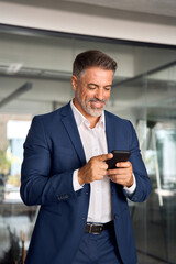 Digital technology application and solutions for business success development. Vertical photo of mature Latin businessman holding smartphone in office. Middle aged manager using cell phone mobile app.