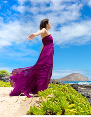 Teen girl in purple dress enjoying breeze on Hawaiian coast