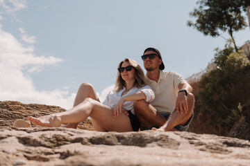 Fototapeta premium Beautiful young loving couple enjoying the scenery while sitting on the rocky mountain together