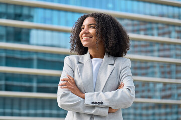 Happy young African American business woman standing in city looking away. Confident smiling...