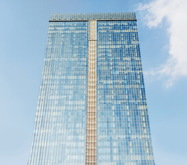 Glass-paneled office building. The glass is blue. Sky background. View from below.