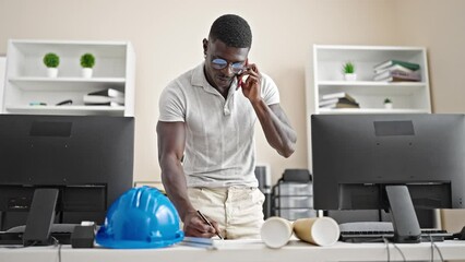 African american man architect talking on smartphone writing on document at the office