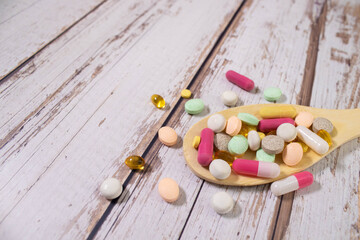 Assorted pharmaceutical medicine pills, tablets and capsules on wooden spoon.