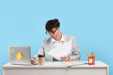 Young man working at white table on light blue background. Deadline concept