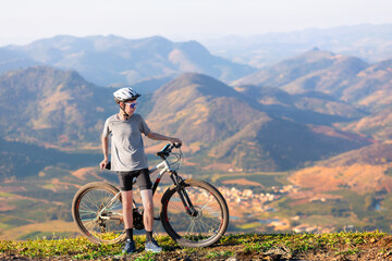 A Brazilian man standing still, taking a break with his mountain bike after cycling. He is at the top of a mountain