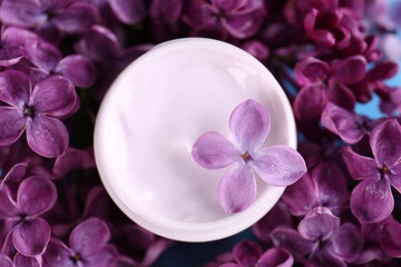 Fototapeta na wymiar Jar of cream and beautiful lilac flowers as background, closeup