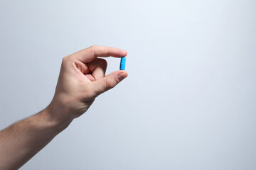 Man holding pill on light grey background, closeup. Space for text