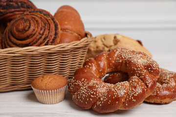 Wicker basket with different tasty freshly baked pastries on white wooden table, closeup