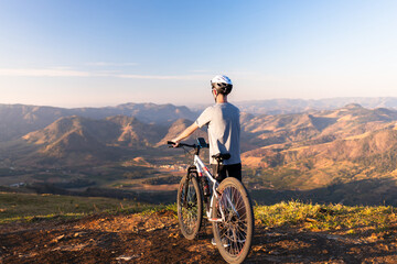 Cyclist resting with his mountain bike while admiring the mountainous landscape in the background.