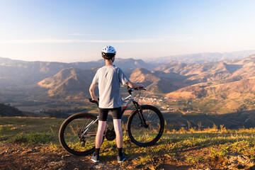 Fototapeta premium Cyclist resting with his mountain bike while admiring the mountainous landscape in the background.