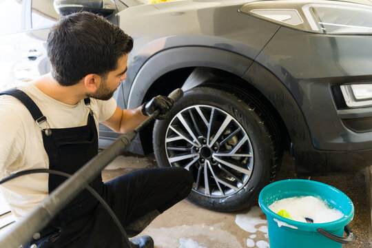 Professional hispanic worker pressure washing car undercarriage