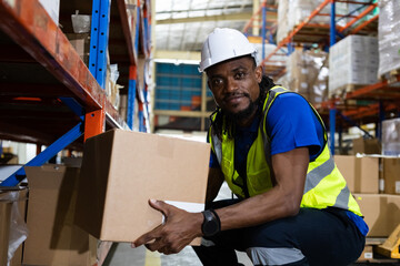 Man american african professional worker wearing safety uniform and hard hat holding box product on shelves in warehouse. Man worker check stock inspecting in storage logistic factory.