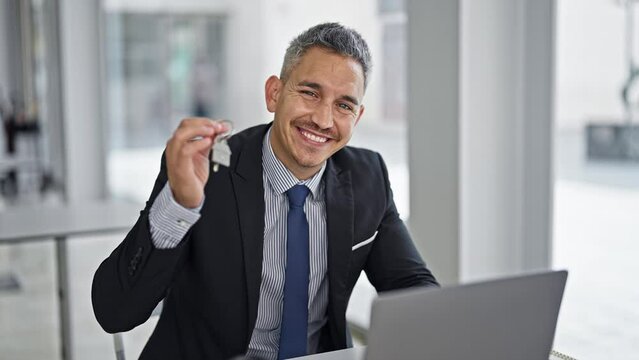 Young hispanic man real state agent holding new house keys using laptop at office