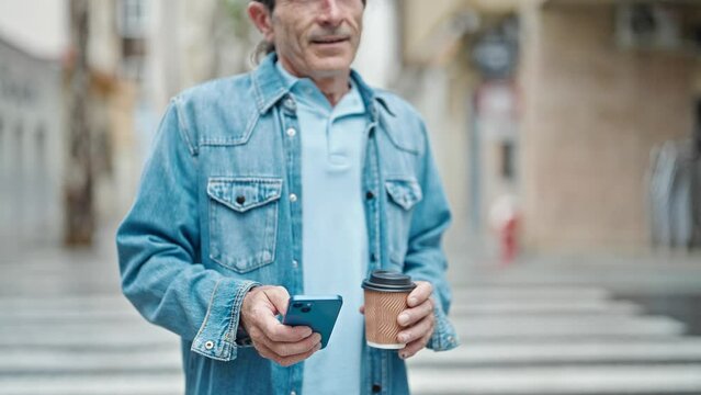 Middle age man using smartphone drinking coffee smiling at street