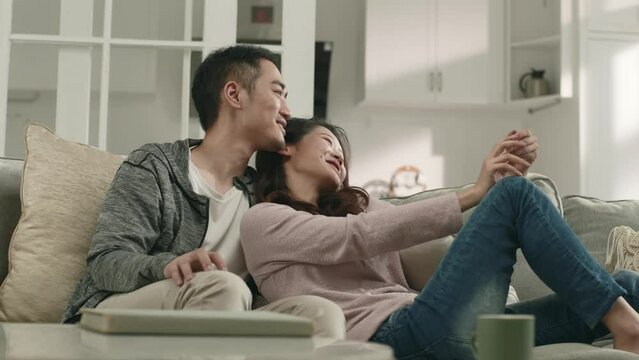 happy young asian couple sitting chatting on family couch at home