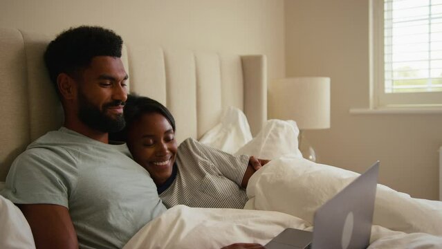 Couple at home in bed streaming movie or show on laptop computer - shot in slow motion