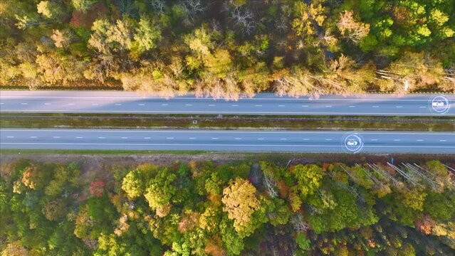 View from above of cars on autopilot self-driving on busy american highway with fast moving autonomous traffic between autumn woods. Future of interstate transportation concept
