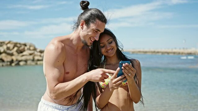Man and woman tourist couple standing together using smartphone at beach
