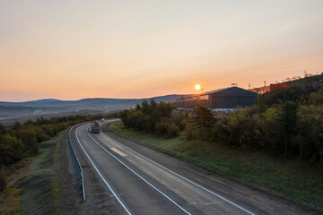 Morning aerial photograph of a highway. Sunrise over asphalt road and industrial buildings. The truck is driving along the road. Kolyma highway, Magadan region, Far East of Russia.