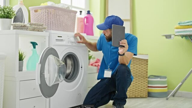 Young hispanic man technician repairing washing machine holding touchpad at laundry room