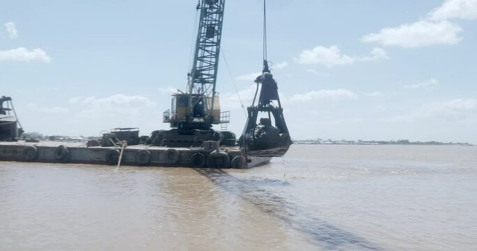 Bucket dredge mounted on a barge removing sediment from one part of a river and put it back in another part of the river 