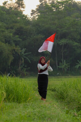 Asian woman in white shirt waving Indonesian flag excitedly in rice field.